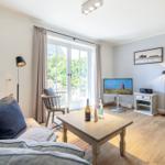 Wohnzimmer mit Sofa, Couchtisch, Fernseher und Kaminofen. Fenster mit Blick auf Garten.