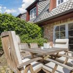 Terrasse mit Holztisch und Stühlen vor einem Haus mit Ziegelfassade und Glasfront.