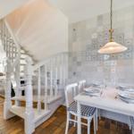 Dining room with table, chairs, and tiled wall. Stairs lead to living area.