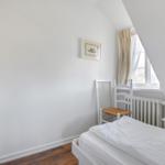 Bedroom with white bed, chair, and window with curtains.