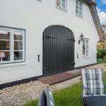 House with white facade, black door, and garden furniture.