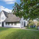 White cottage with thatched roof and garden area with table and chairs.