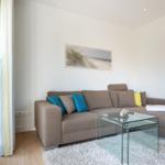 Ein Wohnzimmer mit braunem Sofa, Glas-Tisch und Wandbild.