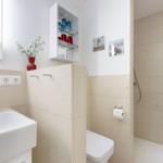 Bad mit Dusche, Waschbecken und Toilette. Wandregal mit Gläsern und Blumen.