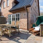 Terrasse mit Holztisch, Stühlen und Liege unter Sonnenschutz.