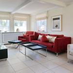 Wohnzimmer mit rotem Sofa, weißen Wänden und Fenstern mit Rollläden.