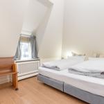 Schlafzimmer mit Doppelbett, Holzboden und Fenster mit Vorhängen.
