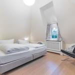 Schlafzimmer mit Doppelbett, schwarzer Ledersessel und schräger Fensterfront.