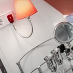 Badezimmer mit Spiegel, Metallbecher und Wandlampe.