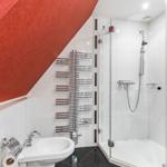 Badezimmer mit Dusche, Waschbecken und Heizkörper an geneigter Wand.