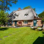 Haus mit Strohdach, Garten mit Liegestühlen und Sonnenschirm.