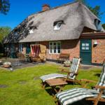 Haus mit Strohdach, Gartenbereich mit Liegestühlen und Terrasse.