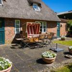 Haus mit strohgedecktem Dach, Garten mit Tisch, Stühlen und Blumenkübeln.