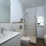 Bathroom with shower, sink, and toilet. Window with plant.