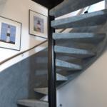 Spiral staircase with blue carpet and two lighthouse pictures on the wall.