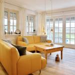 A living room with yellow sofas, wooden table, and windows overlooking the garden.