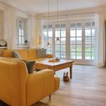 A living room with a yellow sofa, wooden table, and large windows.