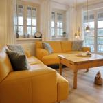 Two yellow sofas with cushions surround a wooden table. Windows and doors offer a view of the garden.