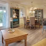 Living and dining area with wooden floor, wicker chairs, and large windows.