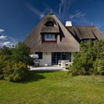 House with thatched roof, terrace, and garden under blue sky.