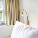 Ein Bett mit Kissen, Wandlampe und Fenster mit Vorhängen.