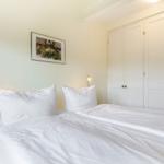 Schlafzimmer mit weißem Bett, Kleiderschrank und Wandbild.