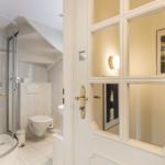 Badezimmer mit Dusche, Toilette und Waschbecken. Tür mit Glasfenstern.