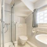 Badezimmer mit Dusche, Toilette und Waschbecken. Fenster mit Vorhang.
