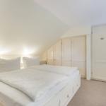 Schlafzimmer mit Doppelbett, weißen Schränken und schrägen Decken.