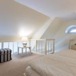 Schlafzimmer mit Dachschräge, Bett, Nachttisch, Lampe und Fenster.