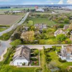 Dorf mit strohgedeckten Häusern und grünen Gärten. Straße führt zum Hafen.
