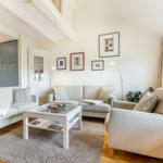 Wohnzimmer mit hellen Sofas, Glas-Tisch und Wandbildern.