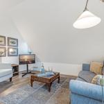 Living room with sofa, armchair, coffee table, and TV under sloped ceiling.