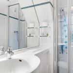 Bathroom with shower, sink, and mirror. Window with view of greenery.