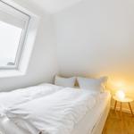 Bedroom with white bed, window, and nightstand with lamp.