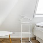 Bedroom with sloped ceiling, bed, coat stand, and table.