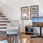 Living area with armchair, TV, and staircase.