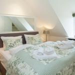 Bedroom with sloped ceiling, bed with green-and-white coverlet, and window with view outside.