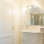 Bathroom with sink, mirror, and shower under sloped ceiling.