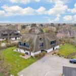 Haus mit Strohdach, Garten und Parkplatz. Blick auf Dorf und Landschaft.
