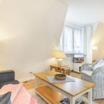 Wohnzimmer mit Sofa, Esstisch und Fernseher. Blick in Schlafzimmer mit Bett.