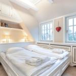 Schlafzimmer mit Doppelbett, weißen Möbeln und Fenstern mit Blick nach draußen.