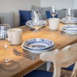 Holztisch mit blau-weißem Geschirr und Stühlen mit blauen Kissen.