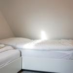Room with two beds and slanted walls. Lighting on the wall.
