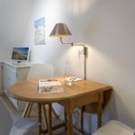 Wooden table with three white chairs, wall lamp, and picture on the wall.