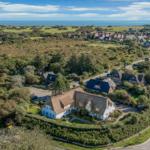 House with thatched roof in green surroundings, view of sea and village.