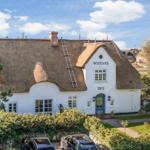 White house with thatched roof and blue door. Garden and parking visible.