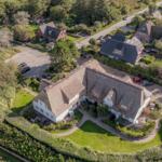 House with thatched roof, surrounded by green areas and paved paths.
