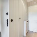 Hall with closet, door, and wall clock. Wooden floor and neutral wall color.