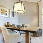 Dining room with wooden table, chairs, and pendant lamp. Pictures hang on the wall.